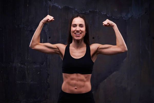 Happy fitness model showing trained biceps isolated against blac — Stock Photo, Image