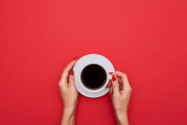 Mãos femininas segurar uma xícara de café forte na área de trabalho vermelha e com — Fotografia de Stock