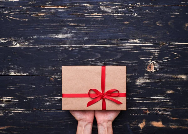 Руки з подарунковою коробкою, загорнуті в коричневий папір і зав'язані червоним ребрами — стокове фото