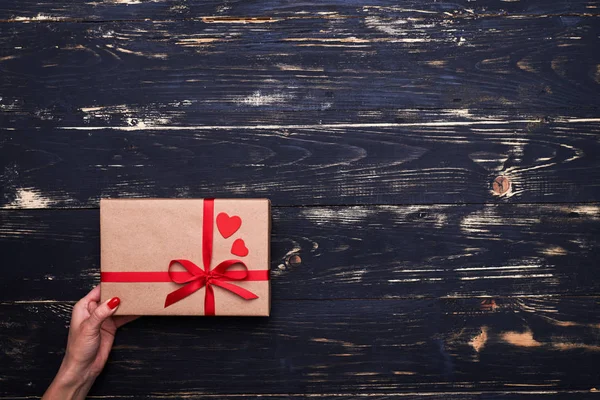 La mano de la mujer sostiene una bonita caja de regalo envuelta con cinta roja — Foto de Stock