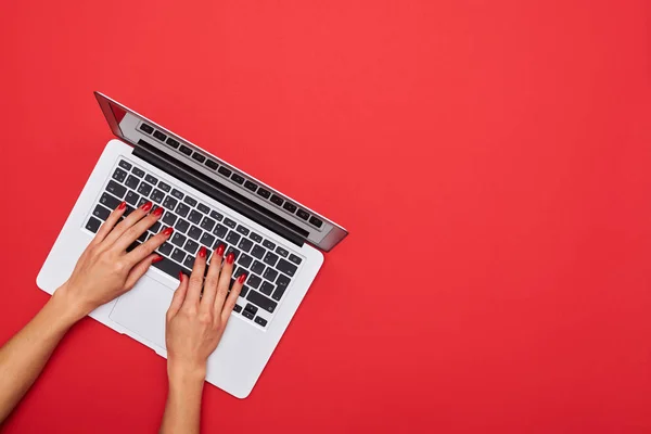 Woman skinny hands working on a silver laptop on a red desktop a — Stock Photo, Image