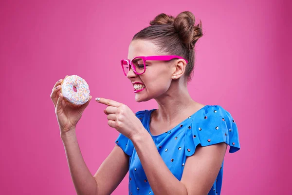 Mulher irritada apontando para o donut sobre fundo rosa — Fotografia de Stock