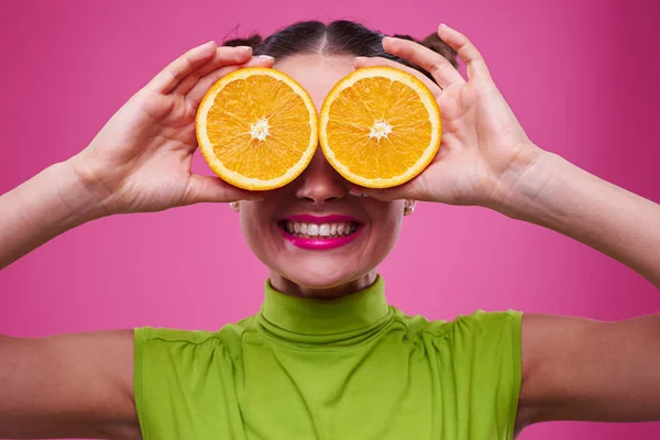 Menina divertida segurando duas partes de laranja perto dos olhos — Fotografia de Stock