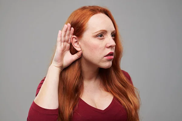 Рыжая женщина держит одну руку возле уха и слушает — стоковое фото