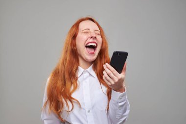 Kızıl saçlı kız cep telefonu tutarken gülüyor 