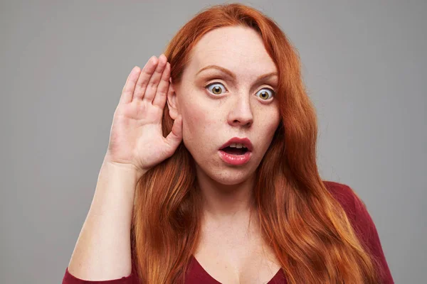 Pelirroja mujer joven escuchando con la mano a la oreja — Foto de Stock