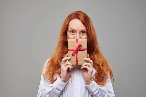 Pleased red hair girl peeps out the present box — Stock Photo, Image