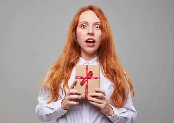 Girl with cooper hair holding a present in an amazement — Stock Photo, Image