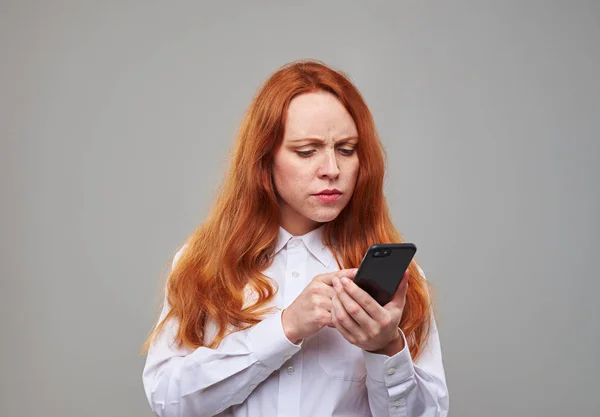 Chica confusa mirando atentamente a la pantalla del teléfono móvil —  Fotos de Stock
