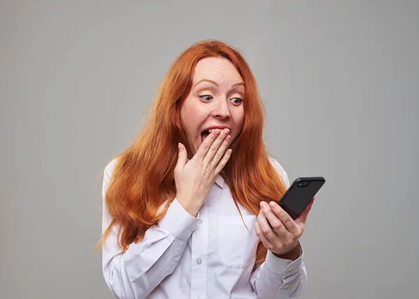 Rood haar tiener scherm van de mobiele telefoon en covers mond kijken — Stockfoto