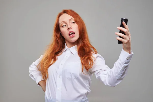 Rödhårig tjej att göra selfie mot grå bakgrund — Stockfoto