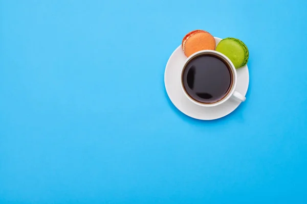 Hands holding a macaroon and a cup of coffee over blue flatlay — Stock Photo, Image