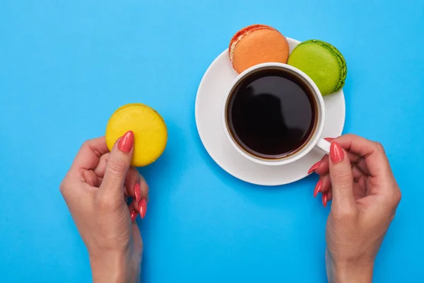 Manos de mujer sosteniendo un colorido galletas y una taza de café ov —  Fotos de Stock