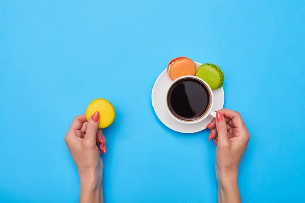 Hands holding macaroon like a perfect match for a cup of coffee — Stock Photo, Image