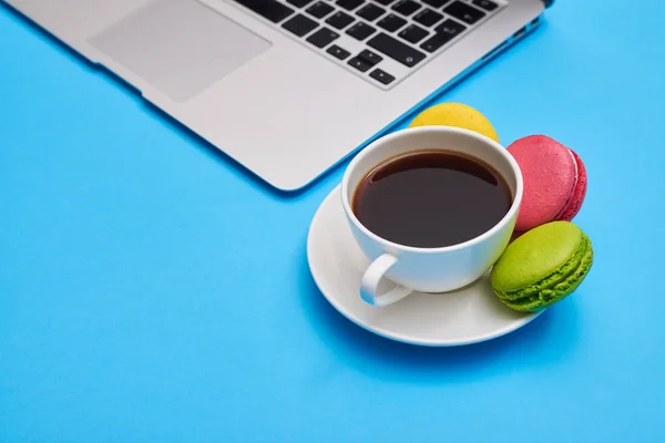 La taza del café con los macarrones en el lugar de trabajo con el portátil — Foto de Stock