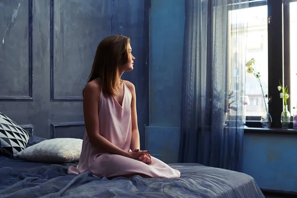 Drömmande flicka i natt-klänning sitter på en säng — Stockfoto