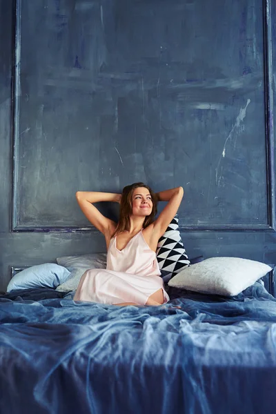 Šťastná dívka sedí na posteli a natahovat ruce ráno — Stock fotografie
