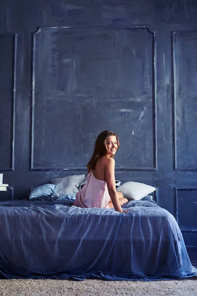 Frestande utseendet på en ung brunett sitter på sängen — Stockfoto