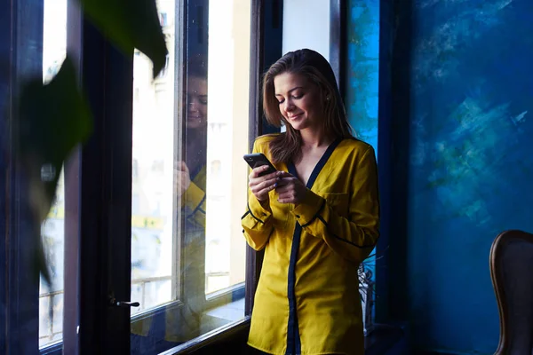 Stijlvolle moderne vrouw stond met mobiele telefoon in de buurt van het venster — Stockfoto
