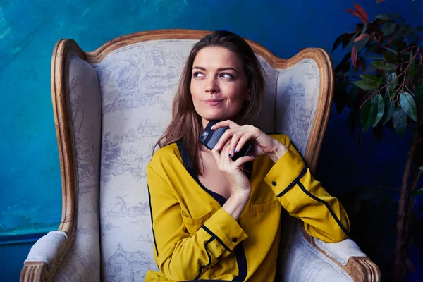 Dreamy young woman holding phone in hands and looking at the win — Stock Photo, Image