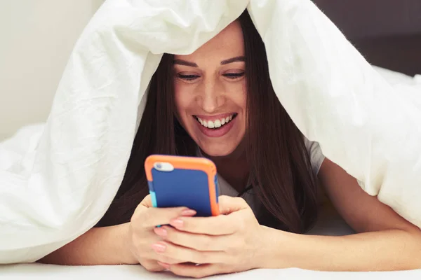 Нежная женщина прячется под одеялом с мобильного телефона — стоковое фото