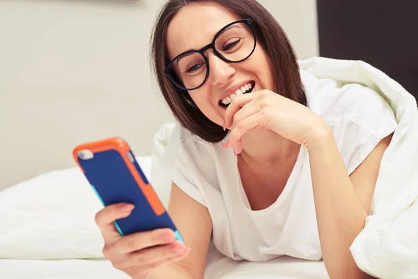 Mulher sorridente em óculos olhando usando telefone celular enquanto está deitado — Fotografia de Stock