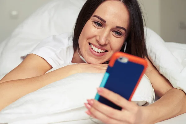 Morena usando el teléfono mientras está acostado en la almohada —  Fotos de Stock