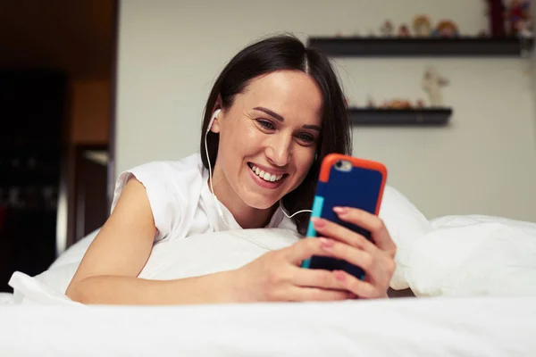 Attraktive Brünette auf dem Bett liegend und Telefon in der Hand — Stockfoto