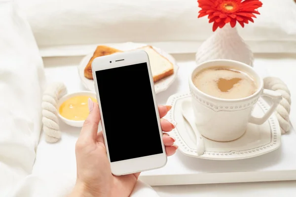 Mão feminina segurando o telefone na mão durante o café da manhã — Fotografia de Stock