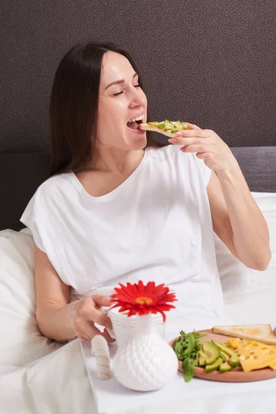 Happy woman in pajamas eats healthy breakfast — Stock Photo, Image