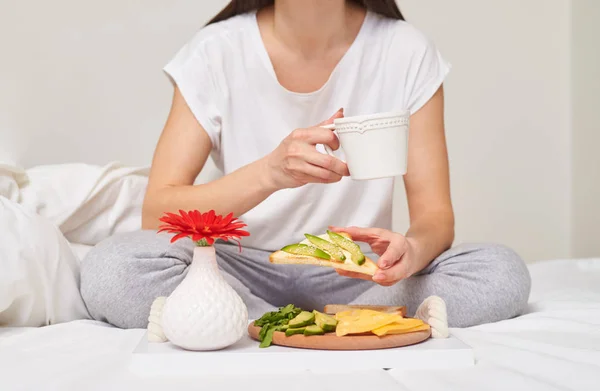 Обрезанный снимок женщины, пьющей чай и поедающей сэндвич — стоковое фото