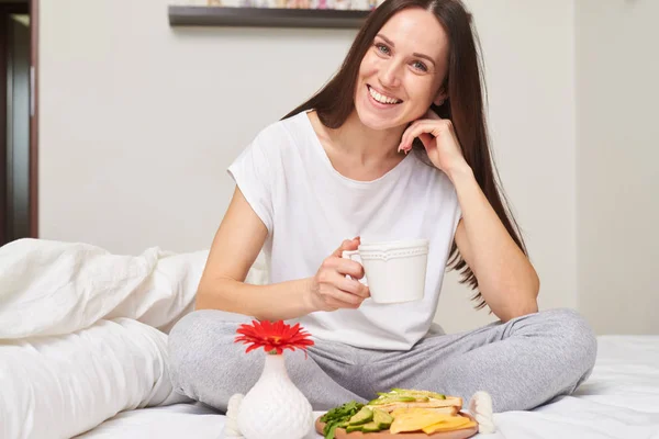 Mulher feliz em pijama desfrutando saudável pequeno-almoço sorri para o seu — Fotografia de Stock