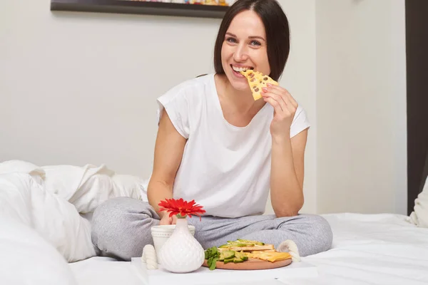 Средний снимок улыбающейся женщины в пижаме, пьющей чай и кушающей — стоковое фото