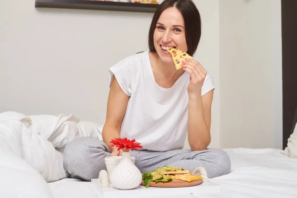 Mitten av skott av leende kvinna i pyjamas dricka te och äta — Stockfoto