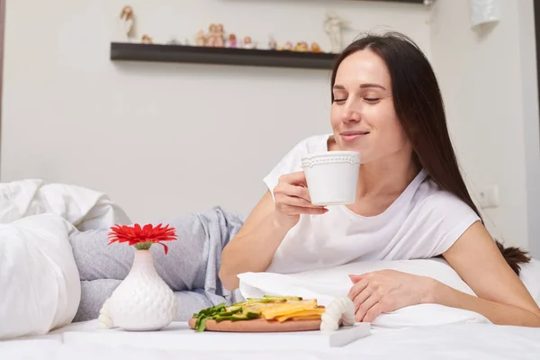 Fantastische Frau riecht traumhaften Tee im Bett liegend — Stockfoto