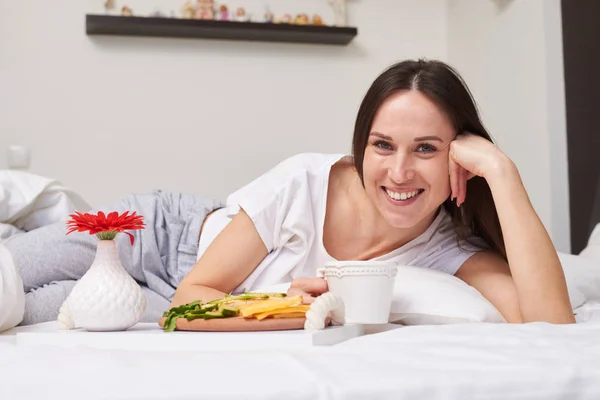 Linda fêmea encontra-se na cama desfrutando de café da manhã — Fotografia de Stock