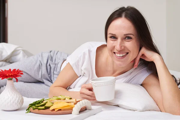 Hermosa morena con pelo largo sosteniendo taza de té mientras está acostada — Foto de Stock