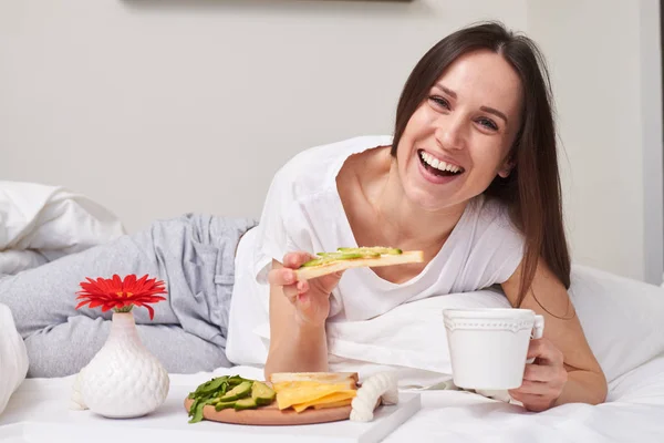 Wanita makan sandwich dengan alpukat di tempat tidur — Stok Foto