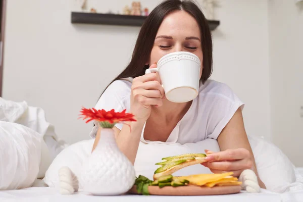 Όμορφη γυναίκα γευσιγνωσία φλιτζάνι αρωματικό και τρώγοντας φρέσκα σάντουιτς — Φωτογραφία Αρχείου