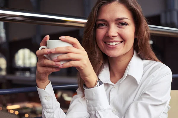 Chica sonriente fina en camisa blanca sosteniendo taza de espresso durante —  Fotos de Stock