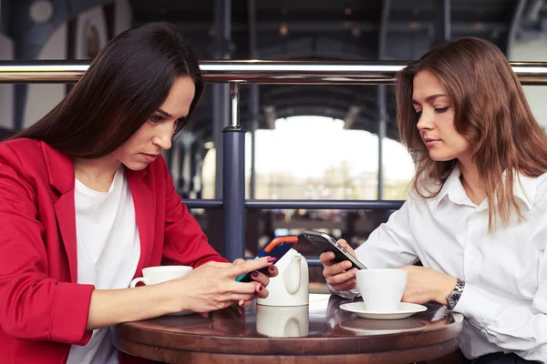 İki güzel konsantre kadın elbiseli smartphones içinde çalışma — Stok fotoğraf