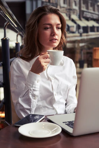 Mujer concentrada con taza de café delante del portátil —  Fotos de Stock