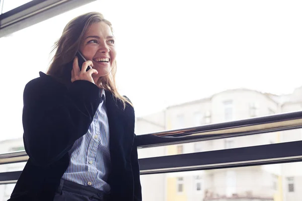 Lachende vrouw met telefoon tegen raam — Stockfoto