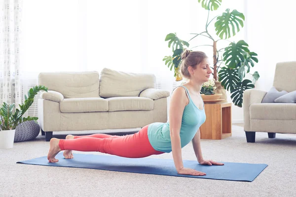 Charming lady doing upward-facing dog pose standing on yoga mat