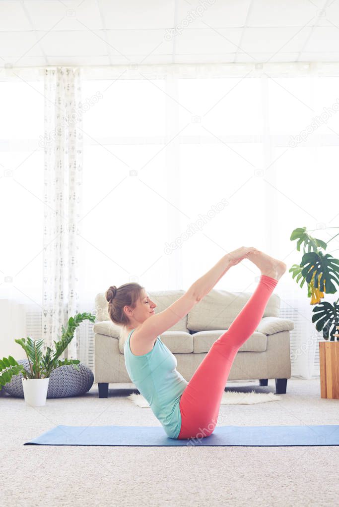Young sportswoman meditating in boat pose on yoga mat