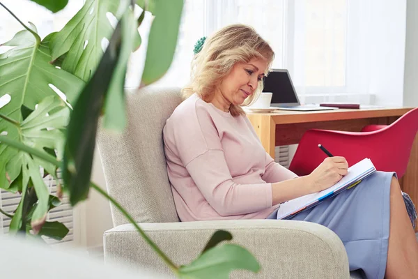 Sierlijke vrouwelijke schrijven geconcentreerd in notitieblok zittend ik — Stockfoto