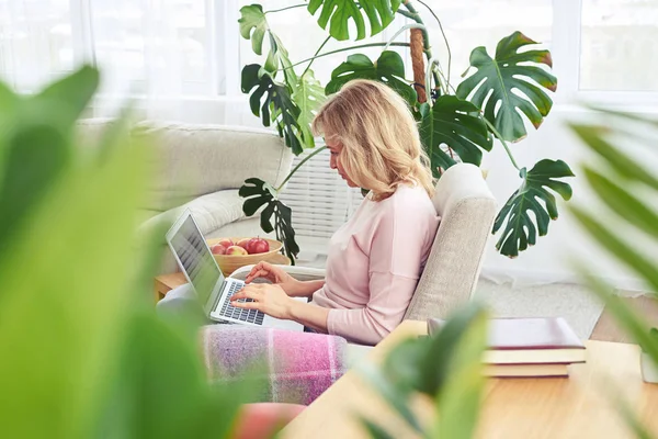 Attraktiv vuxen blondin arbetar i laptop medan du sitter i fåtöljer — Stockfoto