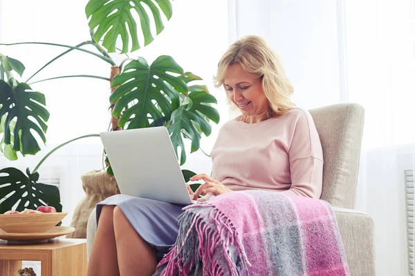 Snygg kvinna utskrift i laptop medan du sitter i fåtölj — Stockfoto