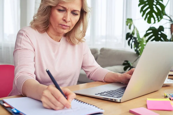 Koncentrerad fru skriva medan du arbetar i laptop — Stockfoto