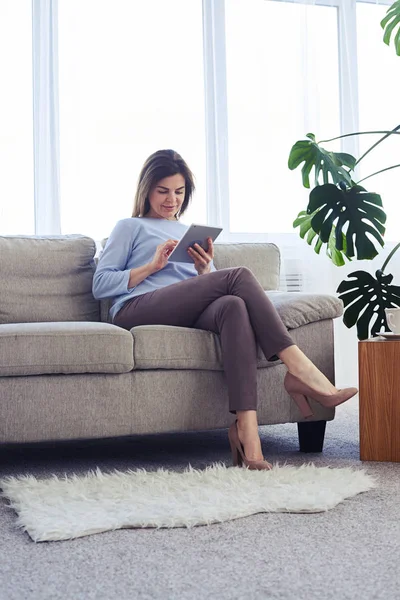 Seriös mogen kvinna som arbetar i laptop medan du sitter på soffan — Stockfoto